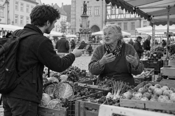 Ein junger Mann nimmt auf dem Wochenmarkt ein Interview mit einer Marktfrau auf