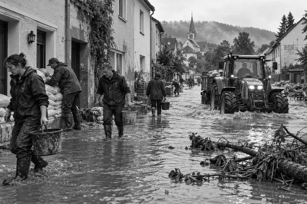 Überflutete Dorfstraße, Anwohner mit Sandsäcken und ein Traktor